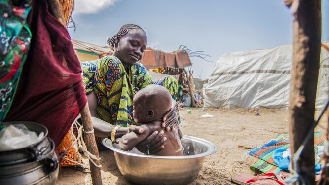 Una mujer baña a un bebé en un campamento de refugiados de Borno.