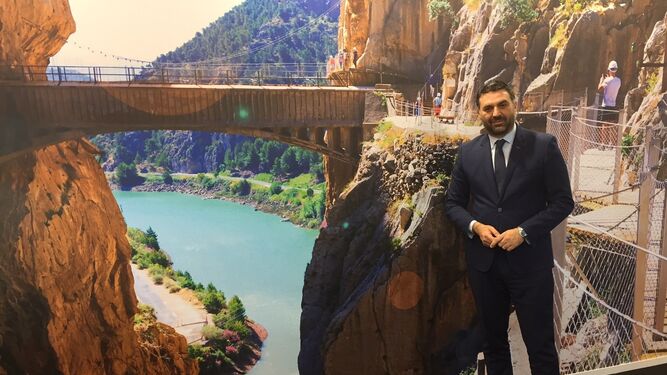 El consejero de Turismo posa tras la entrevista delante de una fotografía del Caminito del Rey en Fitur.