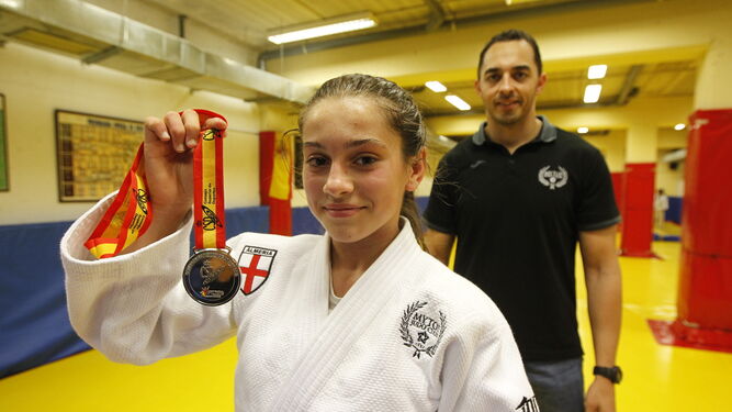 Clara muestra orgullosa su medalla de plata con Miguel Ruiz, su entrenador, a la espalda.
