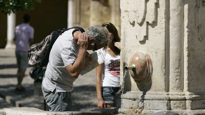 Un hombre se refresca la nuca con el agua de una fuente en la vía pública.