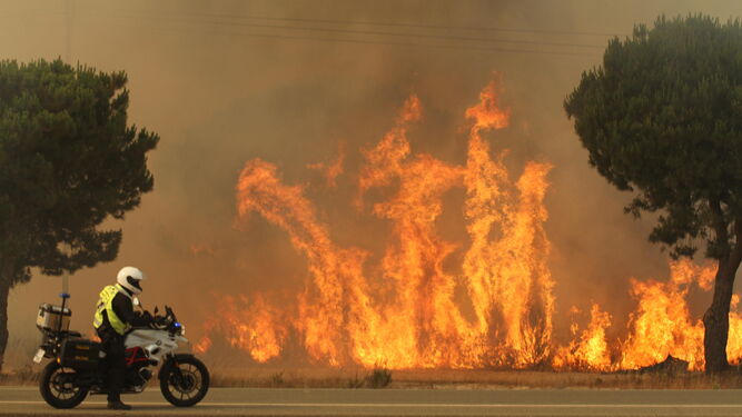 Un efectivo pasa con su moto al lado del incendio en una de las carreteras afectadas.